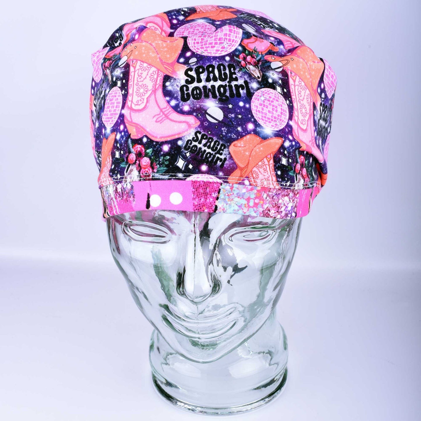 Close-up of the Space Cowgirl scrub cap fabric featuring a vibrant pattern of disco balls, cowboy boots, stars, and crescent moons on a dark background.