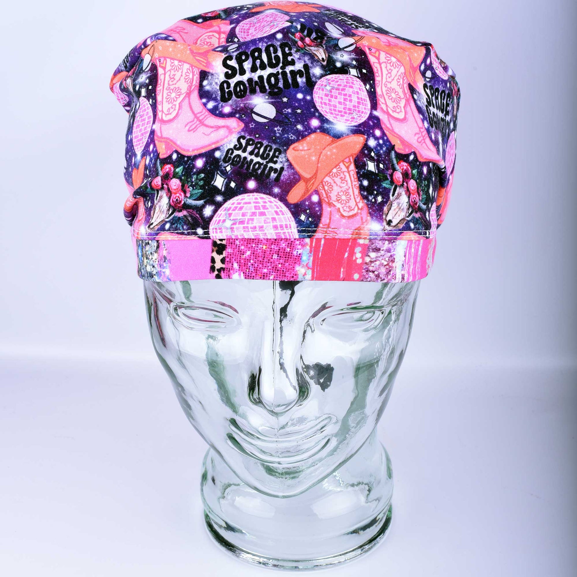 Close-up of the Space Cowgirl scrub cap fabric featuring a vibrant pattern of disco balls, cowboy boots, stars, and crescent moons on a dark background.