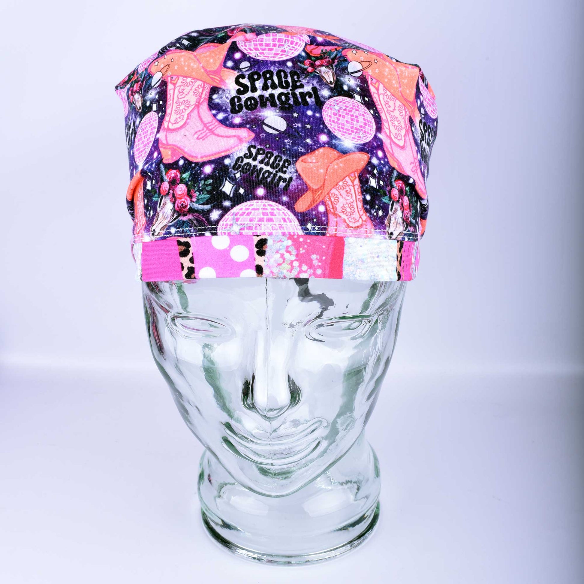 Close-up of the Space Cowgirl scrub cap fabric featuring a vibrant pattern of disco balls, cowboy boots, stars, and crescent moons on a dark background.
