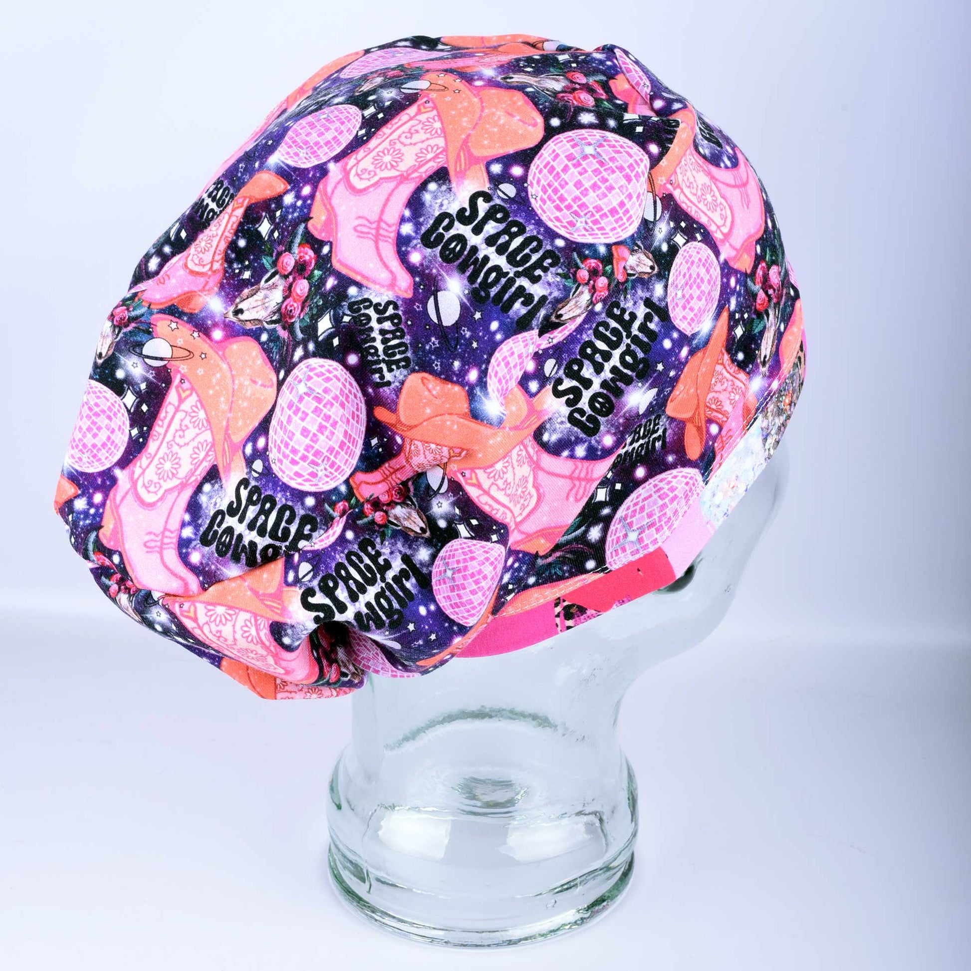 Close-up of the Space Cowgirl scrub cap fabric featuring a vibrant pattern of disco balls, cowboy boots, stars, and crescent moons on a dark background.