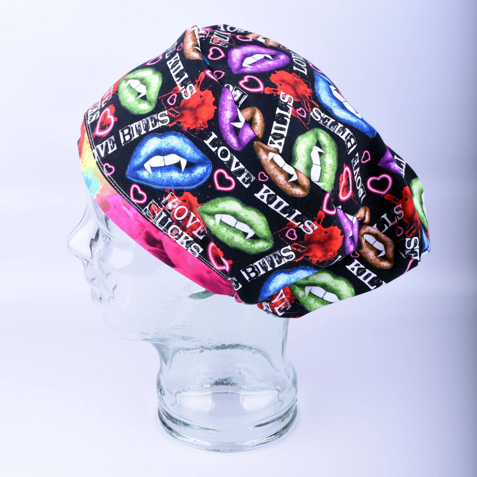 Full-coverage scrub cap featuring an edgy, vibrant Valentine's Day pattern of colorful conversation hearts with phrases like "Love Kills" and "Love Sucks" on a black background, displayed on a clear glass mannequin head.