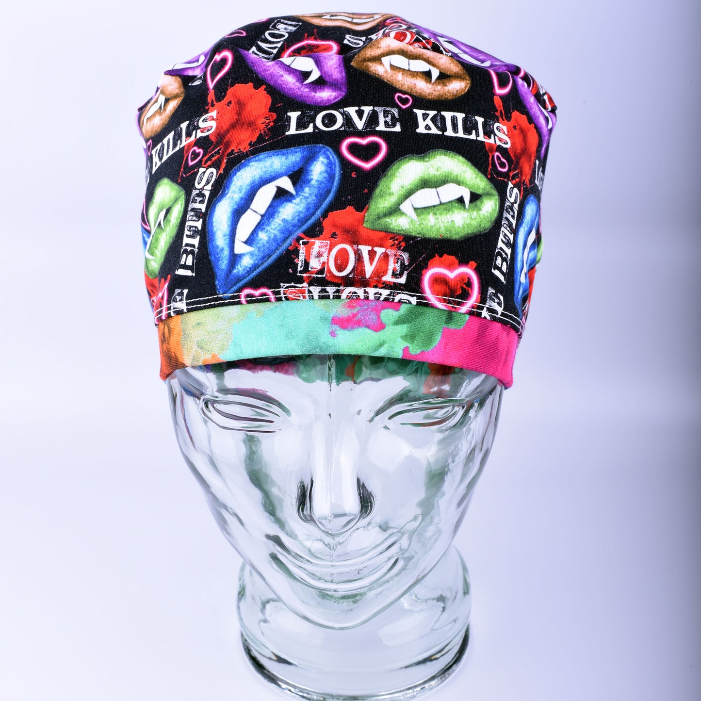Full-coverage scrub cap featuring an edgy, vibrant Valentine's Day pattern of colorful conversation hearts with phrases like "Love Kills" and "Love Sucks" on a black background, displayed on a clear glass mannequin head.