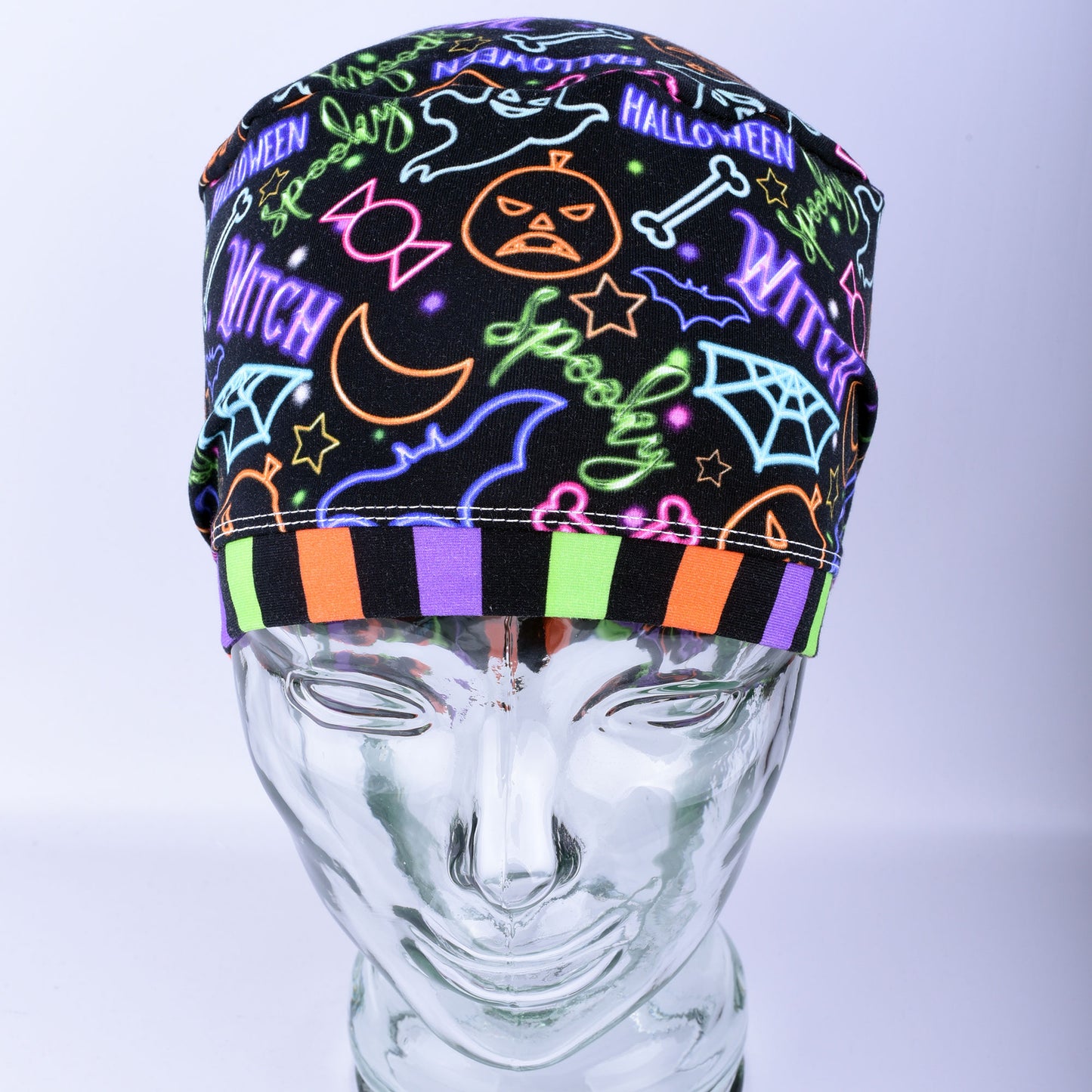 Front  view of a stretchy medical scrub hat featuring a bright neon Halloween print with witch hats and pumpkins.