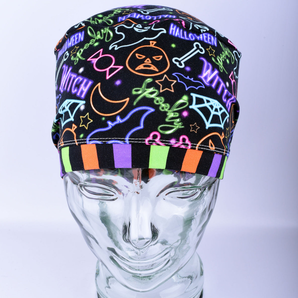 Front  view of a stretchy medical scrub hat featuring a bright neon Halloween print with witch hats and pumpkins.
