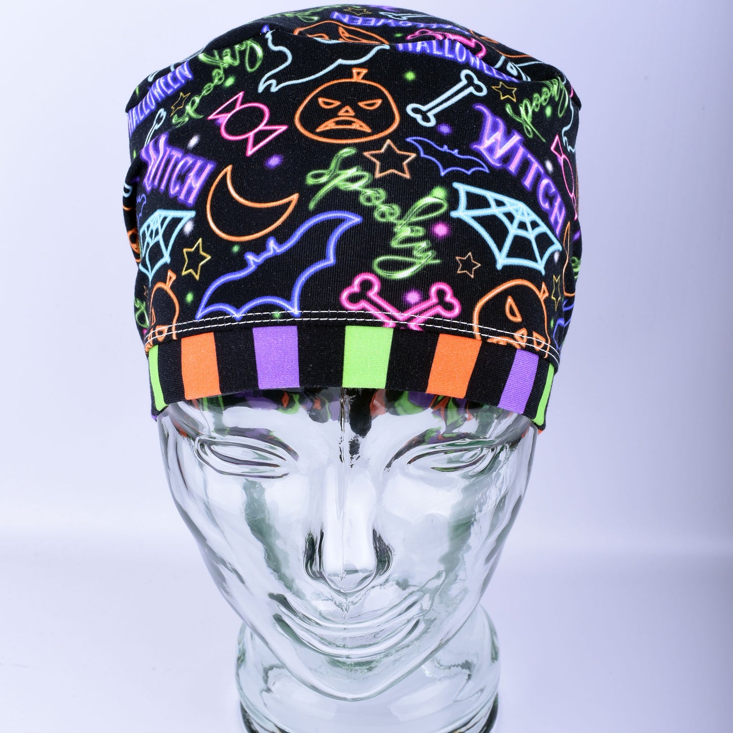 Front  view of a stretchy medical scrub hat featuring a bright neon Halloween print with witch hats and pumpkins.
