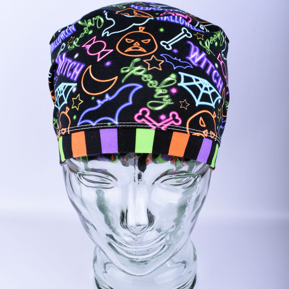 Front  view of a stretchy medical scrub hat featuring a bright neon Halloween print with witch hats and pumpkins.