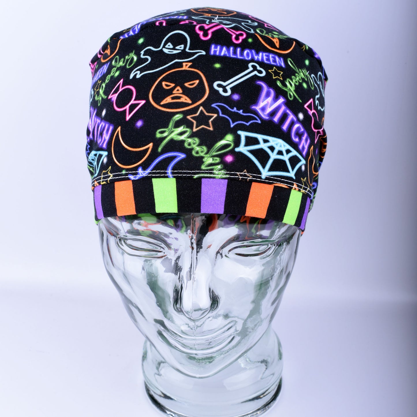 Front  view of a stretchy medical scrub hat featuring a bright neon Halloween print with witch hats and pumpkins.