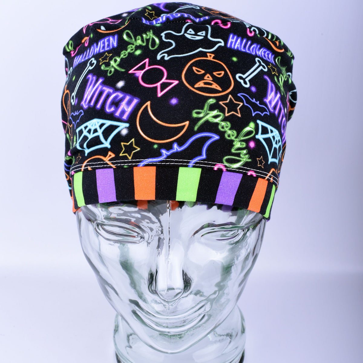 Front  view of a stretchy medical scrub hat featuring a bright neon Halloween print with witch hats and pumpkins.