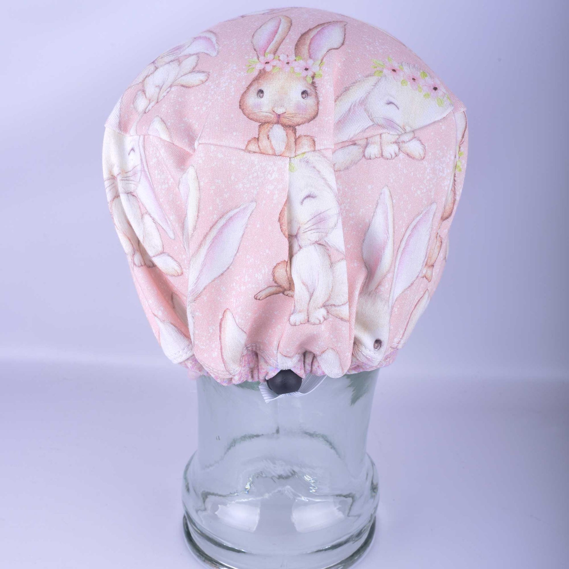 Back view of a sweet bunnies scrub cap featuring hand drawn bunnies and pink flowers with a cord lock toggle for adjusting size. 