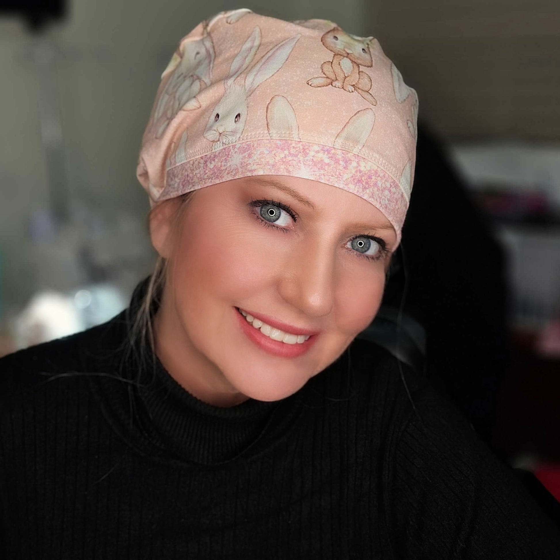 Woman wearing a pink scrub cap with rabbit designs, smiling.