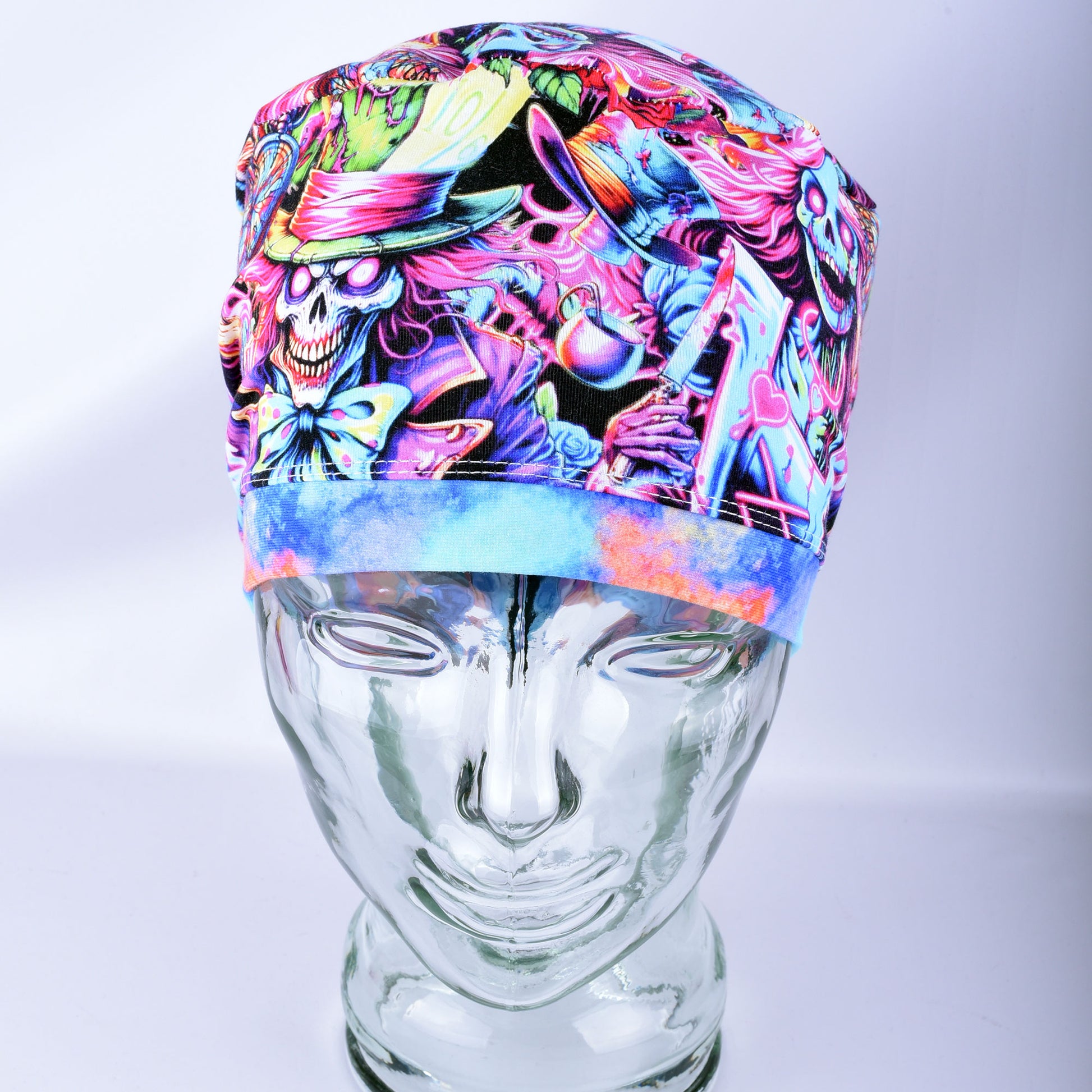 A colorful medical scrub cap with a vibrant, multicolored psychedelic print featuring cartoon skulls, hats, and abstract patterns, displayed on a clear glass mannequin head against a light gray background.