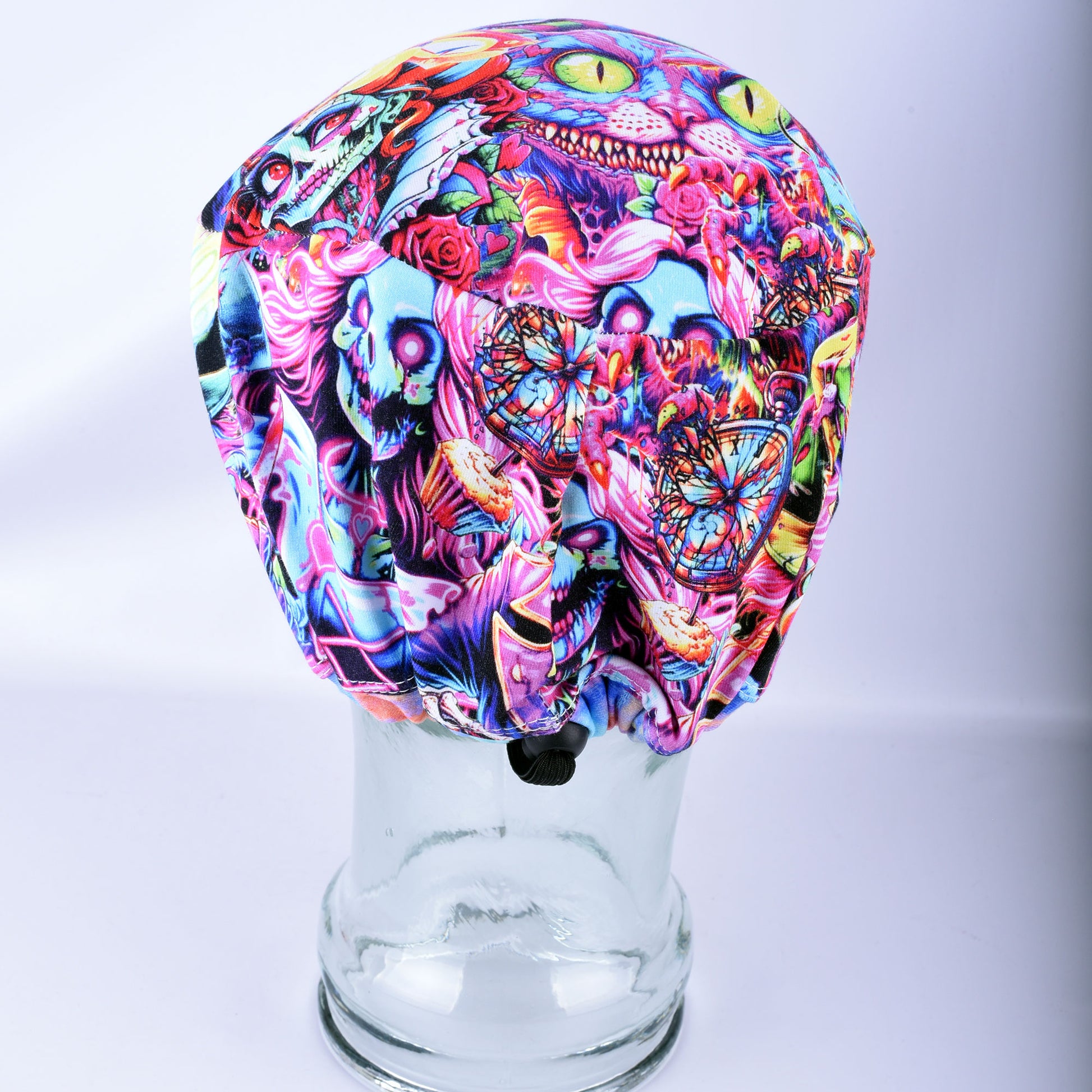 A multicolor novelty scrub cap featuring a vibrant, chaotic collage print of the cats, skulls, roses, zombies and butterflies, displayed on a clear glass mannequin head against a light gray background.