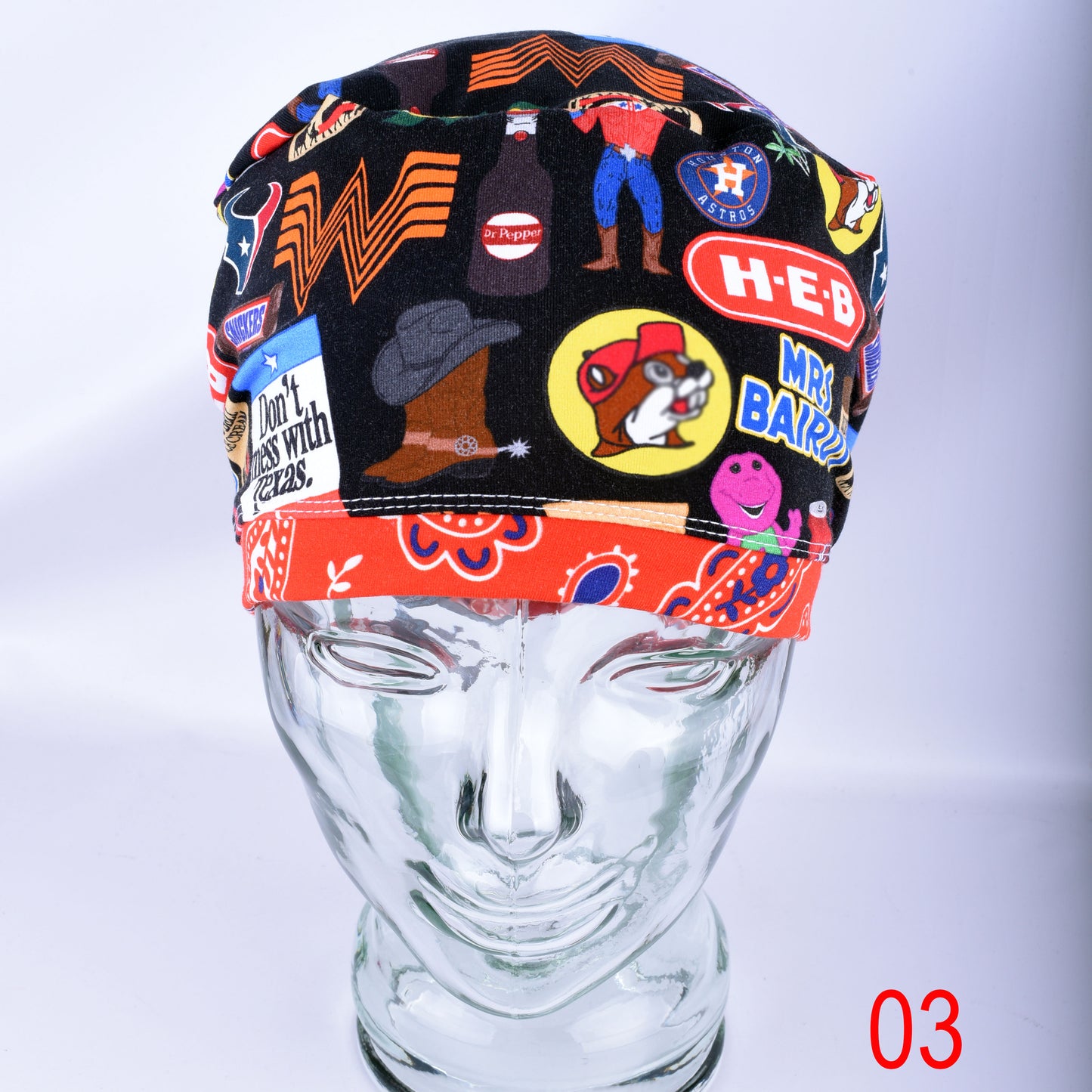 A multicolor novelty scrub cap displayed on a clear mannequin head. The scrub hat features a black base with various colorful patches, logos, and illustrations including a cowboy hat, a bear, and Texas themed elements.