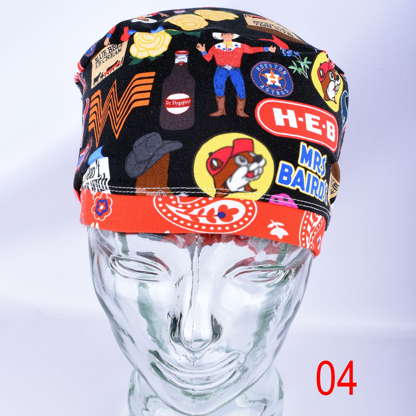 A black fabric surgical cap with a colorful retro cartoon print, displayed on a clear mannequin head. The cap features illustrations of a cowboy, a dog, a bottle, and various Texas themed elements.