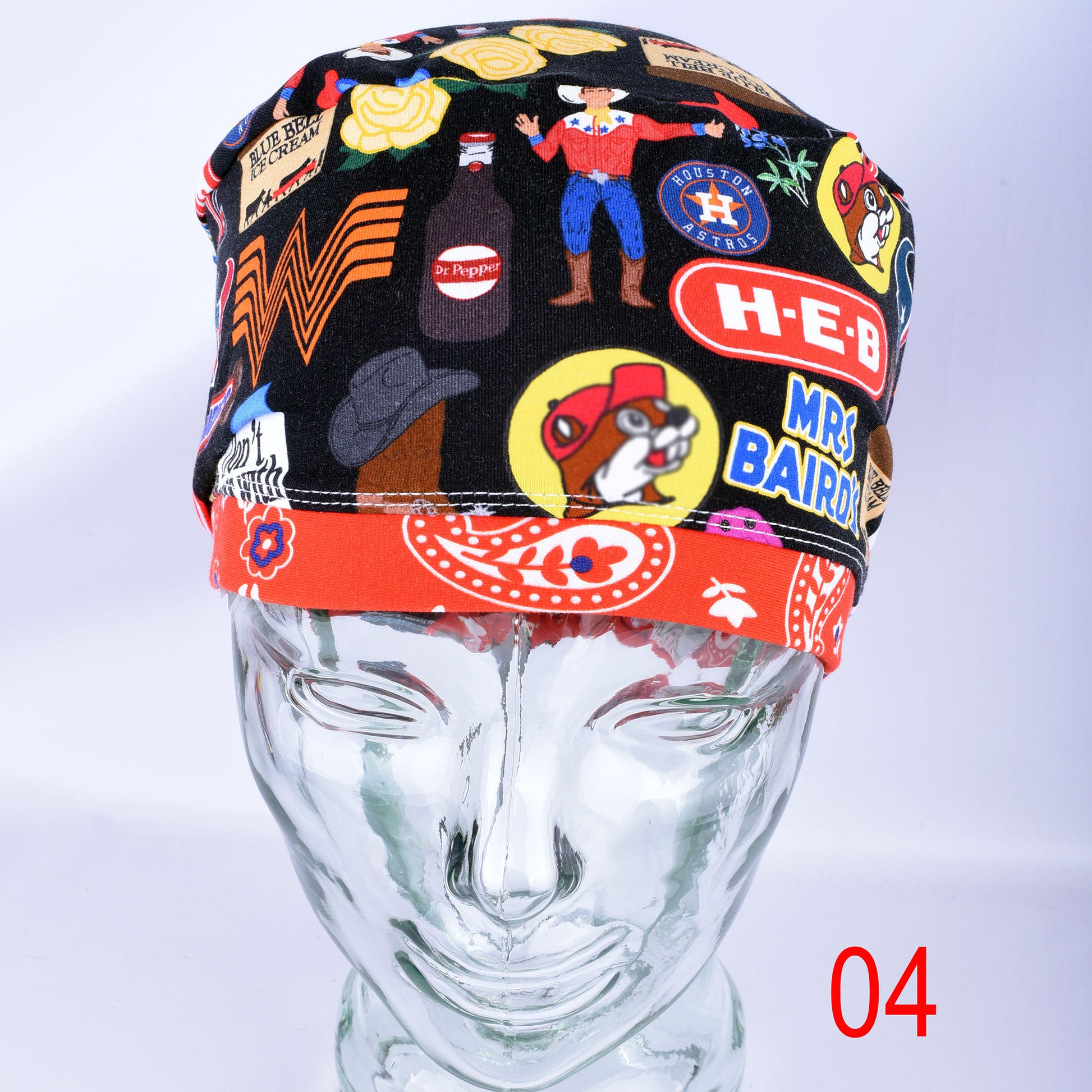 A black fabric surgical cap with a colorful retro cartoon print, displayed on a clear mannequin head. The cap features illustrations of a cowboy, a dog, a bottle, and various Texas themed elements.