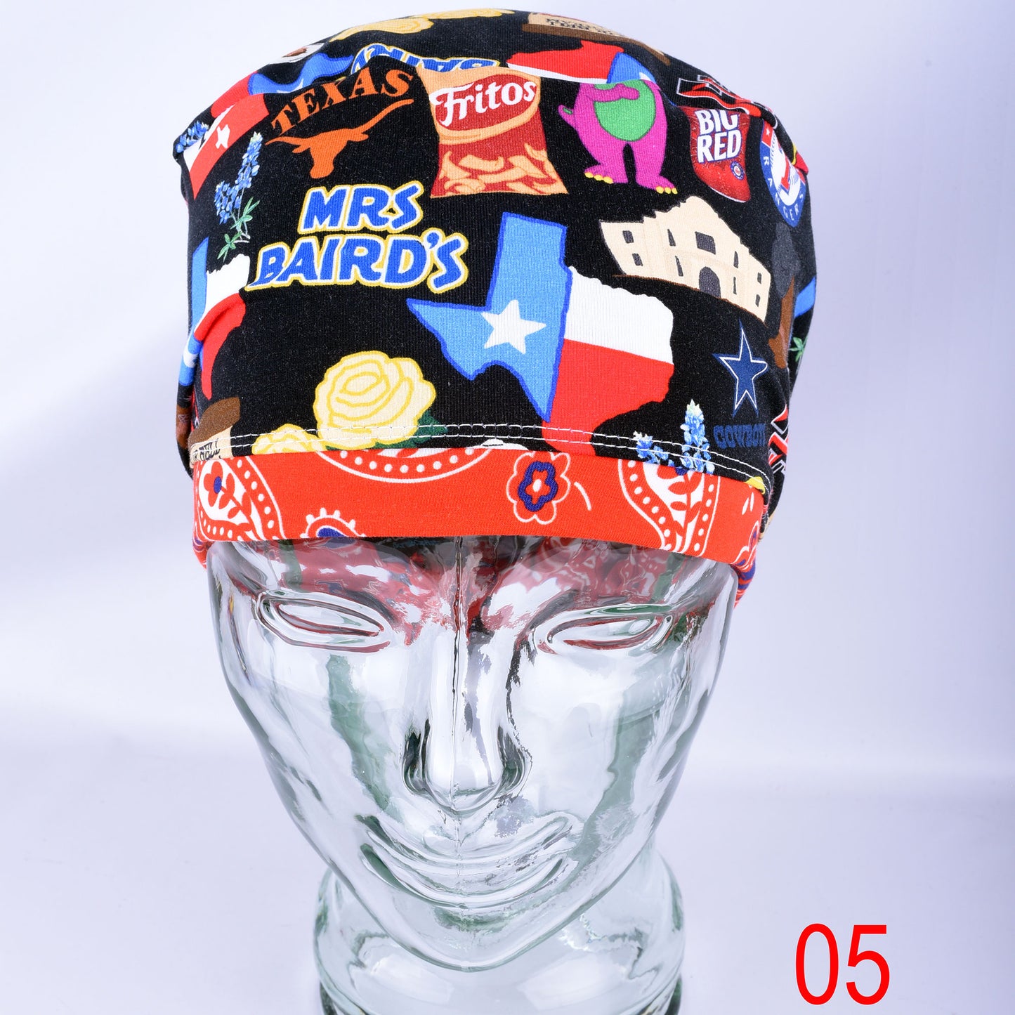 A black scrub cap with a colorful Texas-themed patchwork print and a red paisley band, displayed on a clear glass mannequin head against a light background.