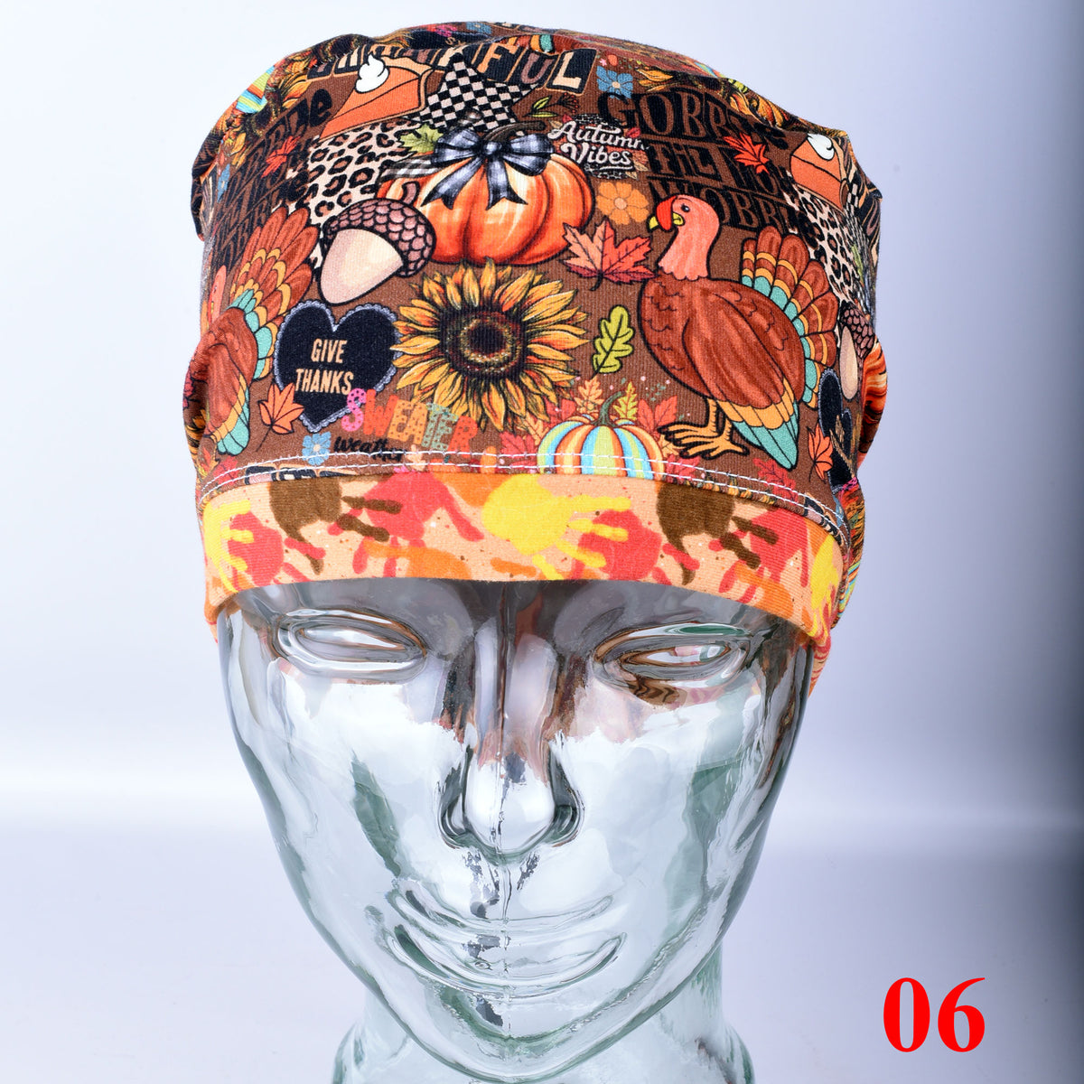 A multicolor Thanksgiving-themed scrub cap displayed on a clear mannequin head. The cap features a busy pattern of pumpkins, sunflowers, turkeys, acorns, and autumn leaves, with a solid orange-yellow patterned brim.