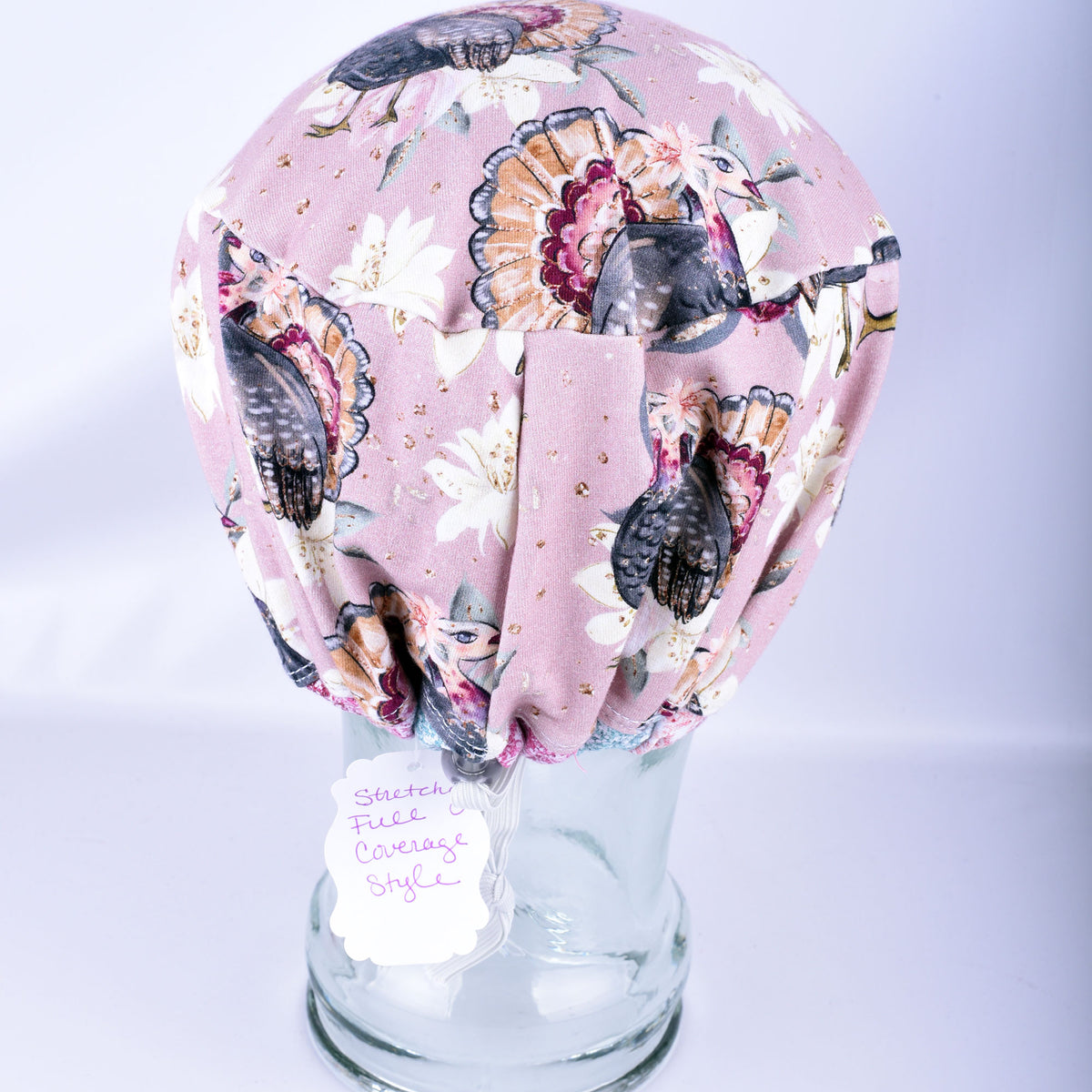 A surgical cap with a detailed turkey and floral pattern, displayed on a clear glass mannequin head.