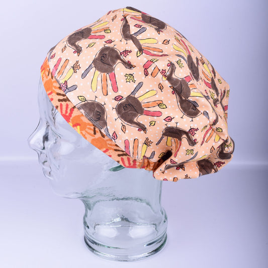 Colorful scrub cap with handprints and turkeys on a mannequin head against a light gray background