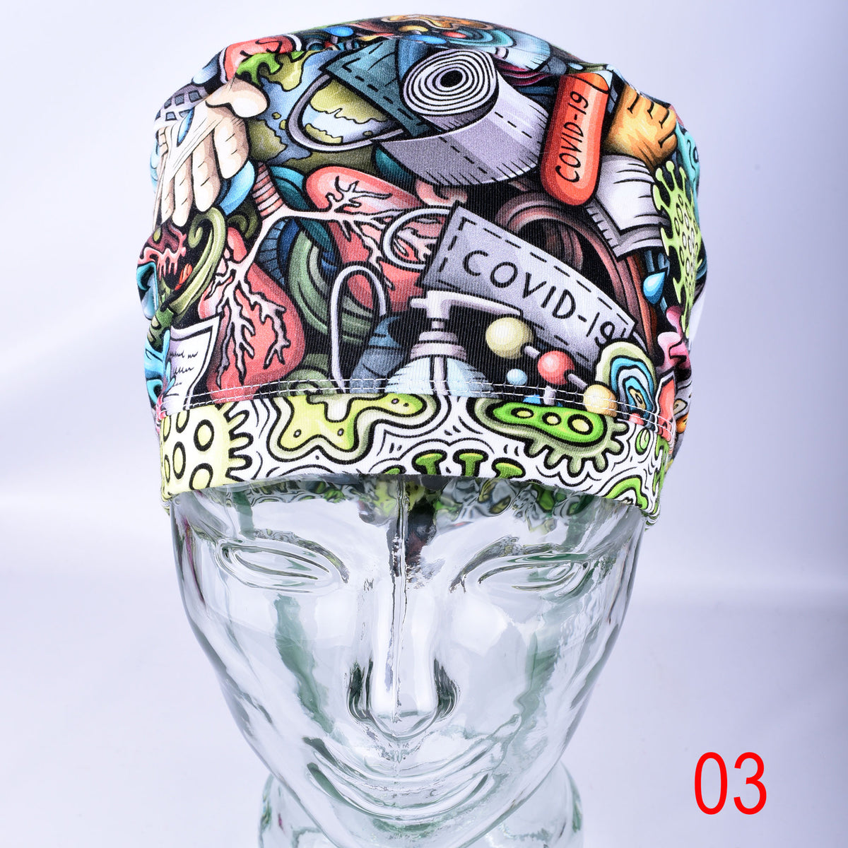 A multicolor medical scrub cap with a detailed cartoon-style illustration featuring medical tools, a stethoscope, a syringe, and text like 'COVID-19', displayed on a clear glass mannequin head against a light gray background.