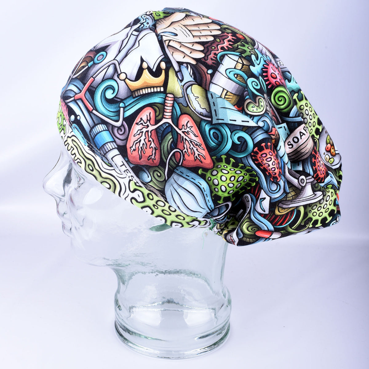 A multicolor medical-themed scrub cap with a detailed cartoon illustration of lungs, a stethoscope, a crown, and other healthcare symbols, displayed on a clear glass mannequin head against a light gray background.