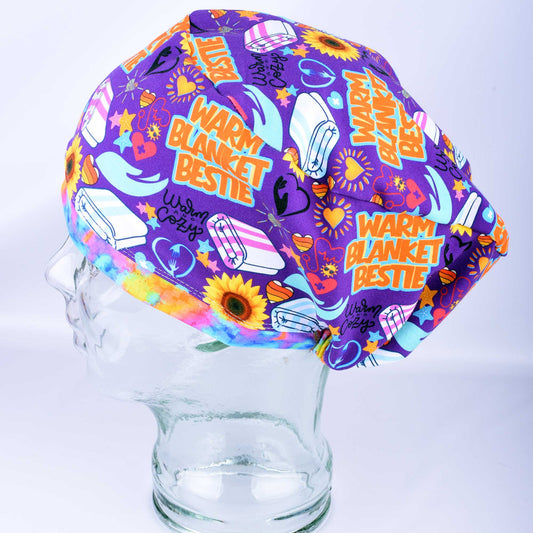 A purple medical scrub cap with a colorful 'Warm Blanket Bestie' pattern, displayed on a clear glass mannequin head against a white background.