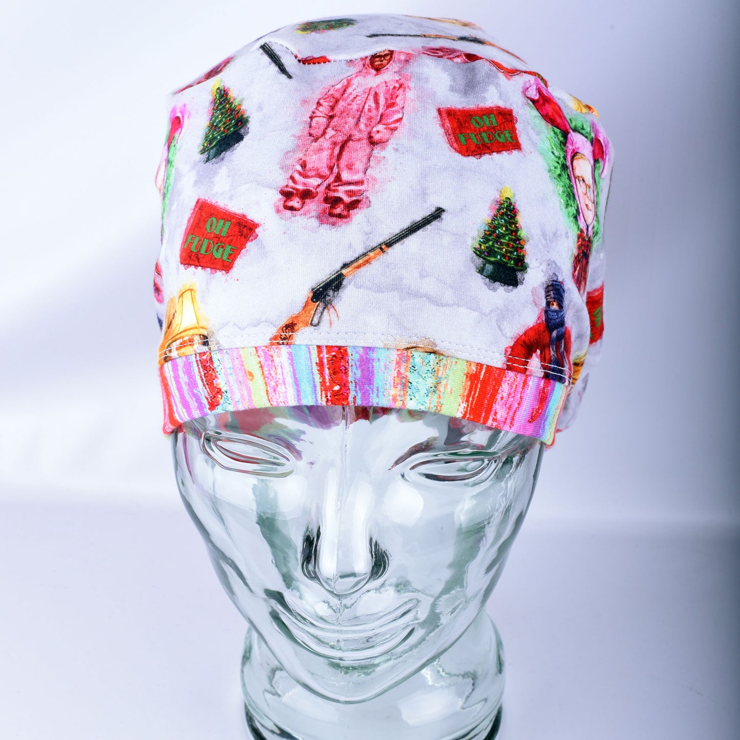A soft stretchy scrub hat with colorful Christmas  holiday-themed designs, displayed on a clear glass mannequin head against a light gray background.