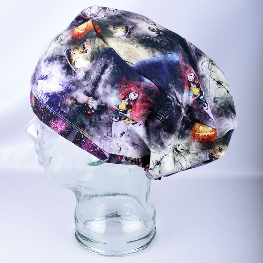 A scrub cap with a dark, colorful cartoon character ghosts print displayed on a clear glass mannequin head against a light gray background.