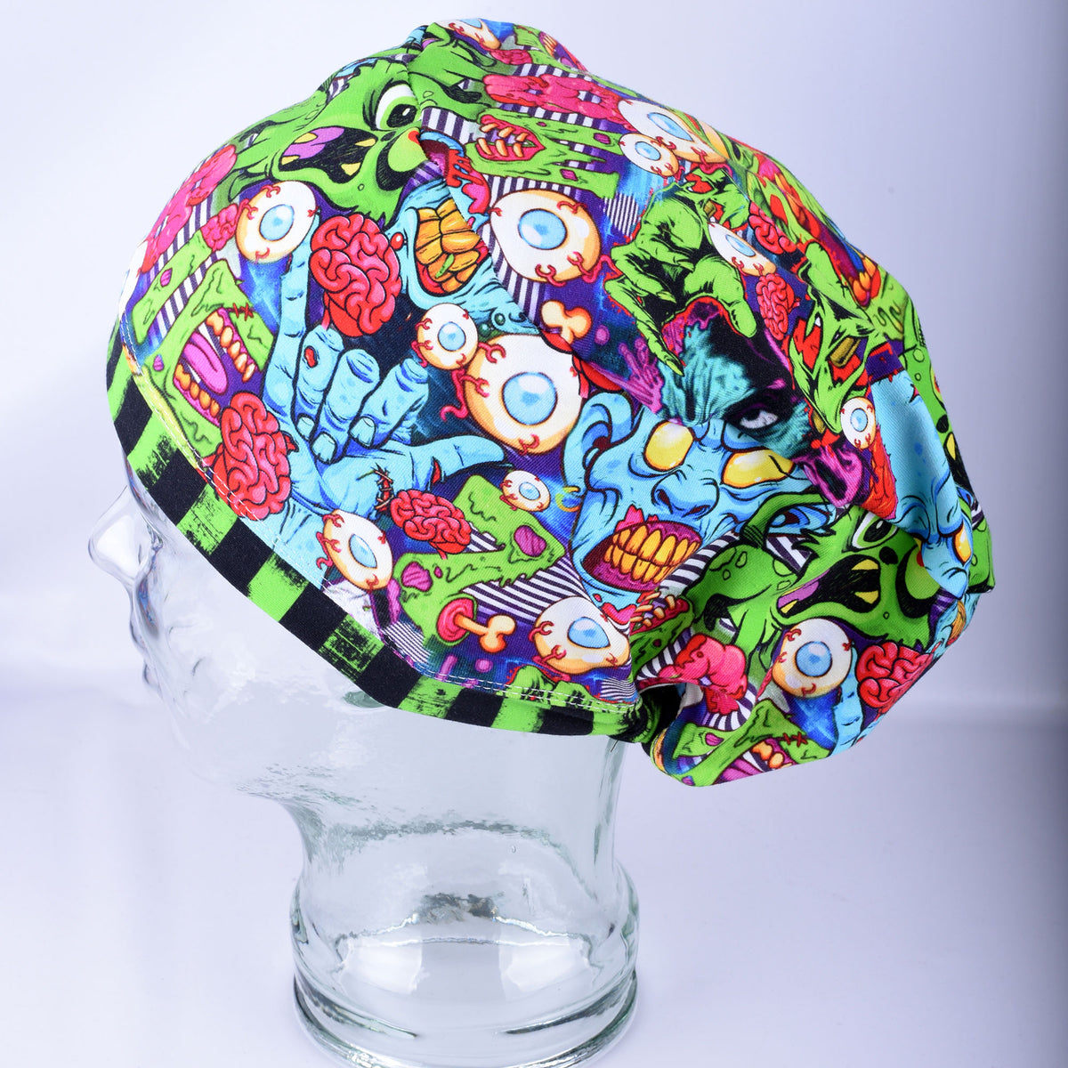 Front view of a full-coverage medical scrub cap with a colorful neon zombie and brain print on a black background, displayed on a mannequin.