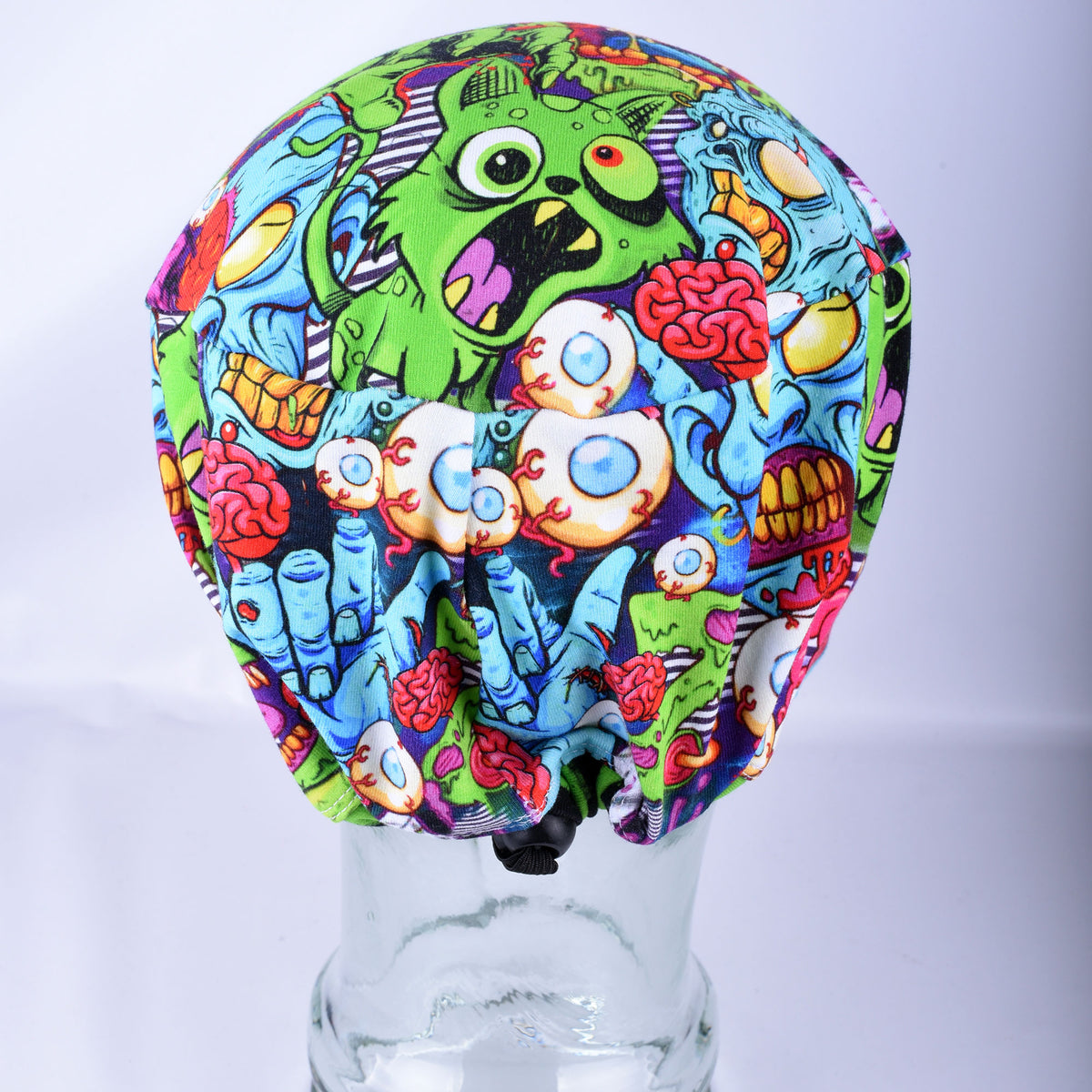 Back view of a full-coverage scrub cap with a vibrant neon zombie pattern and an encased elastic back with a toggle clasp.