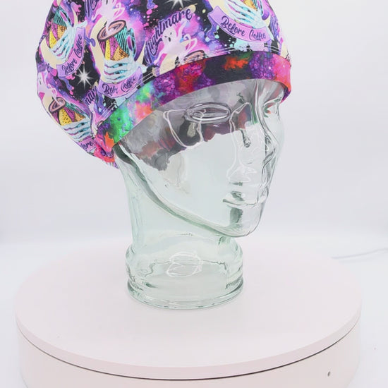 Video showcasing a 360-degree rotating view of the Nightmare Before Coffee full-coverage scrub cap on a clear mannequin head, highlighting the vibrant purple caffeine-themed pattern and adjustable rear toggle fit.