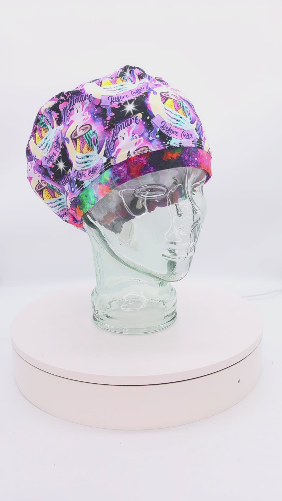 Video showcasing a 360-degree rotating view of the Nightmare Before Coffee full-coverage scrub cap on a clear mannequin head, highlighting the vibrant purple caffeine-themed pattern and adjustable rear toggle fit.