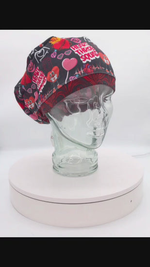 360-degree video showcase of the Heart Throb Squad scrub cap on a clear mannequin head, displaying the vibrant red, black, and pink cardiology-themed anatomical heart pattern and full-coverage fit.