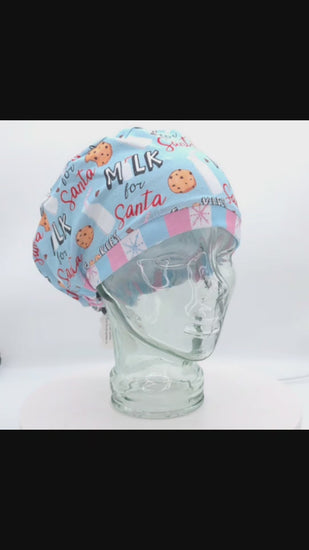 360-degree rotating video of a clear mannequin head displaying a full-coverage scrub cap featuring a light blue festive print with chocolate chip cookies, glass milk bottles, pink accents, and "Milk for Santa" text.