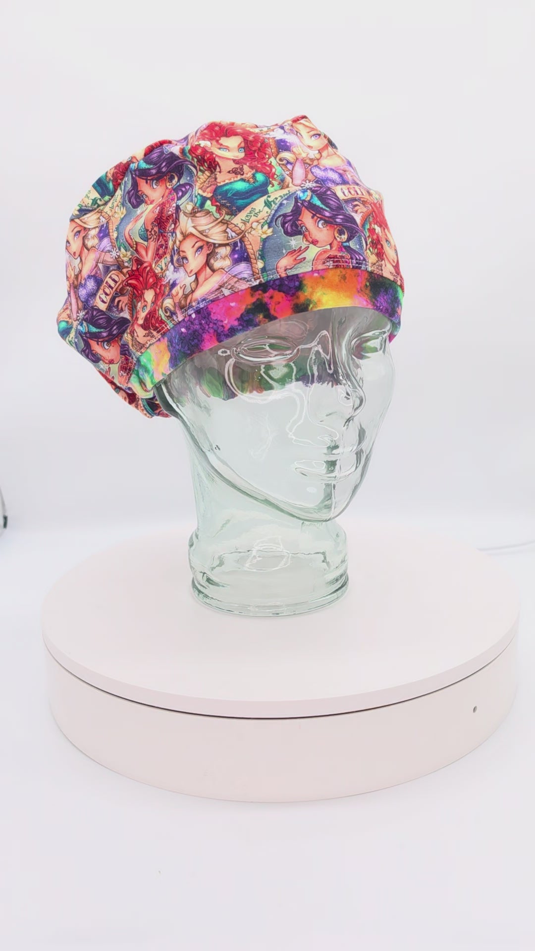 A 360-degree rotating view of a Tattoo Princess full-coverage Euro-style scrub cap on a clear mannequin head. The premium cotton knit fabric features an edgy royal design with colorful illustrations on a clean white background.
