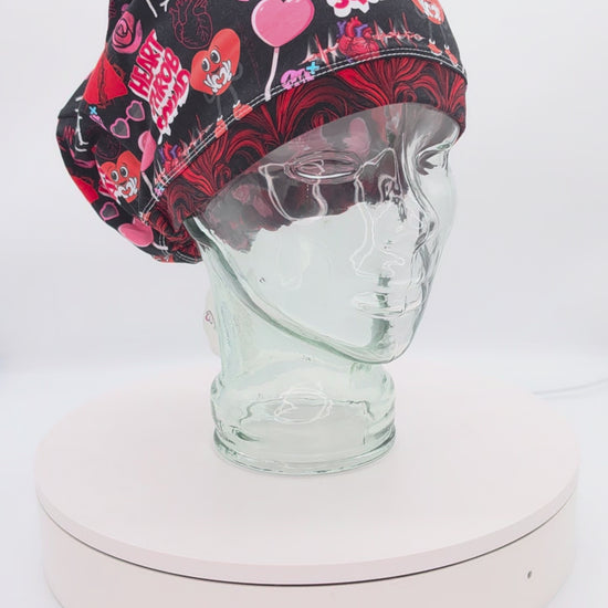 360-degree video showcase of the Heart Throb Squad scrub cap on a clear mannequin head, displaying the vibrant red, black, and pink cardiology-themed anatomical heart pattern and full-coverage fit.