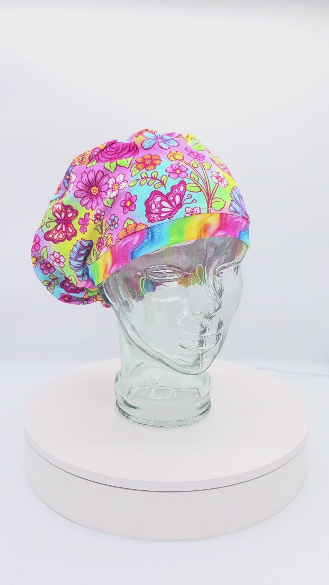 360-degree rotating video of the Butterflies and Flowers Euro-style scrub cap on a clear mannequin head, displaying the colorful floral and butterfly print, adjustable toggle, and full coverage fit.