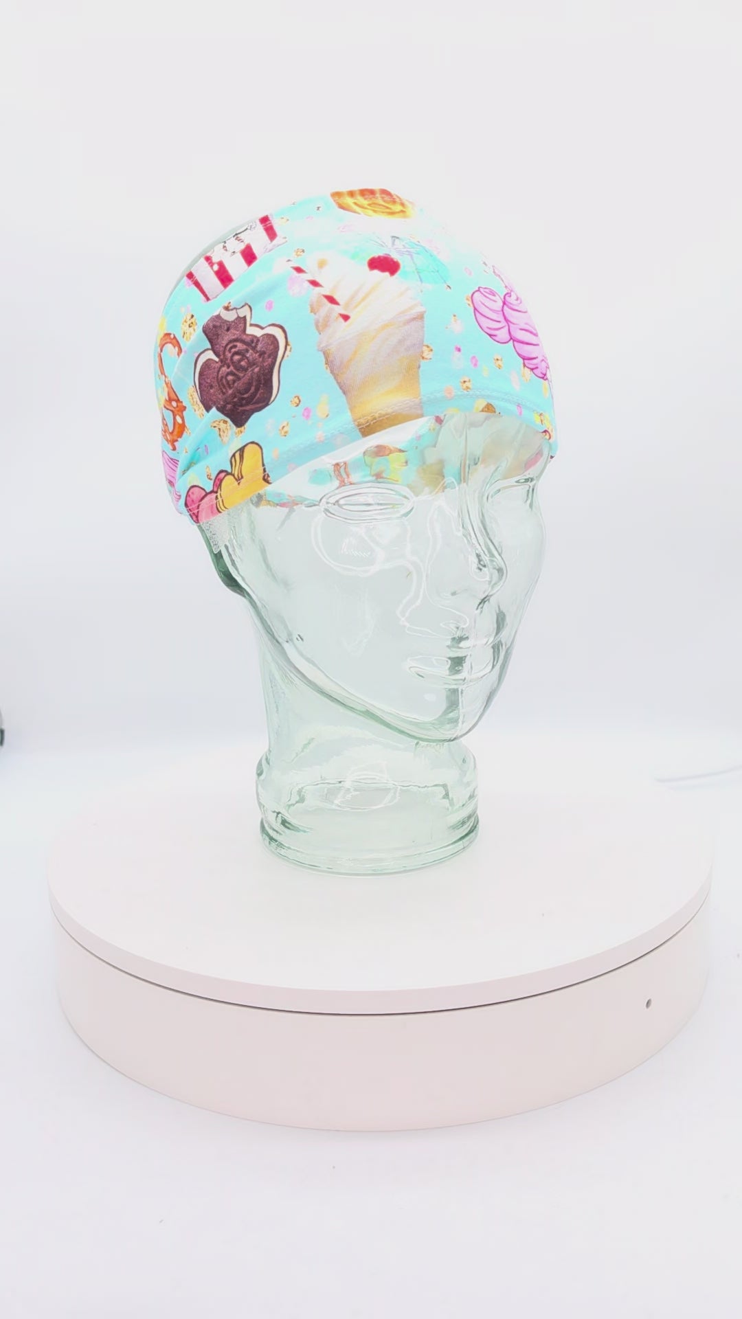 Video showcasing a 360-degree rotating view of the Magical Snacks wide headband on a clear mannequin head, highlighting the vibrant theme park treats pattern and adjustable cord-lock toggle fit.