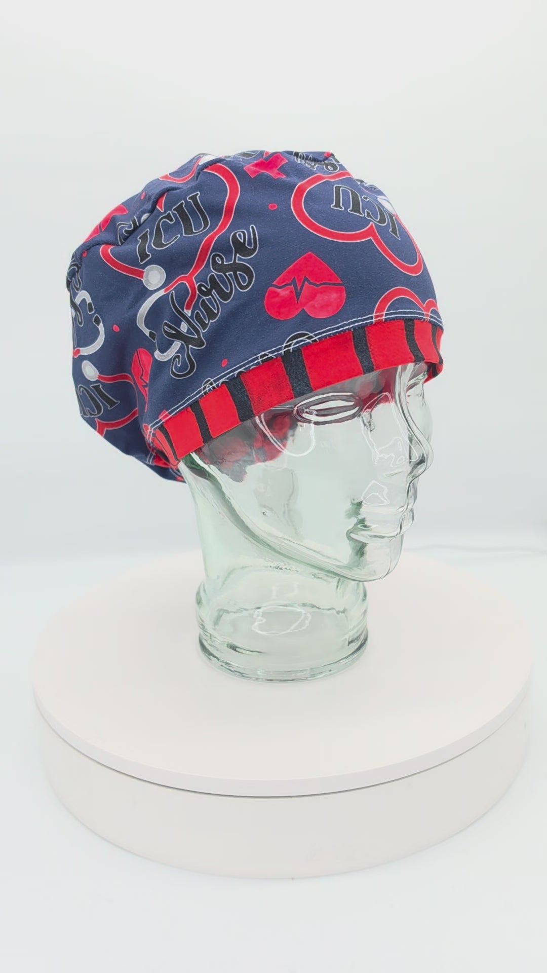 360-degree rotating view of the ICU Nurse Full Coverage Scrub Cap on a clear mannequin head, showcasing the navy blue background, red and blue medical graphics, and adjustable back toggle.