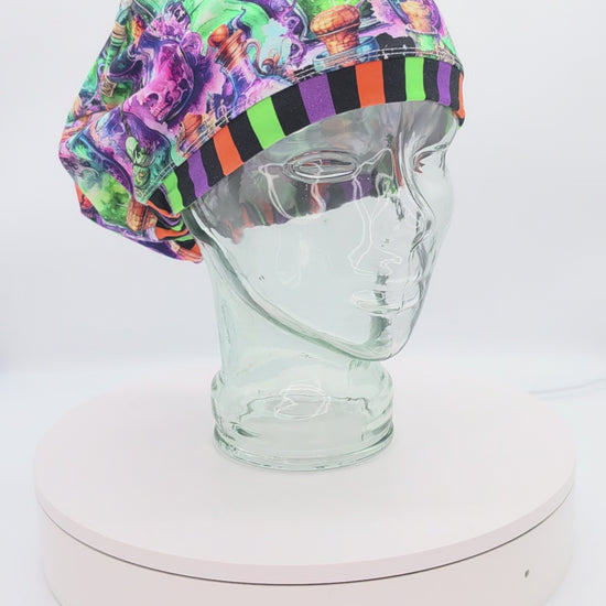 Video showcasing a 360-degree rotating view of the Halloween Potions Euro-style scrub cap on a clear mannequin head, highlighting the vibrant potion bottle pattern and adjustable toggle drawstring fit.