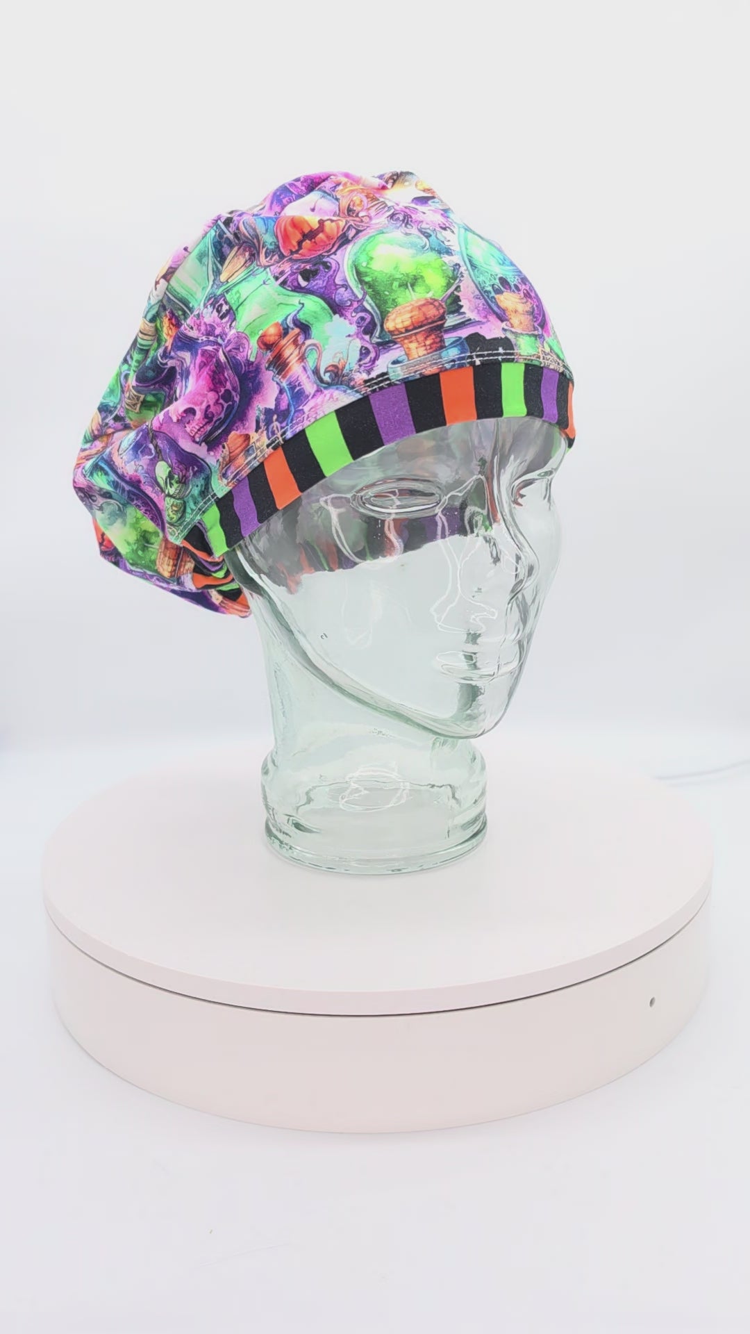 Video showcasing a 360-degree rotating view of the Halloween Potions Euro-style scrub cap on a clear mannequin head, highlighting the vibrant potion bottle pattern and adjustable toggle drawstring fit.