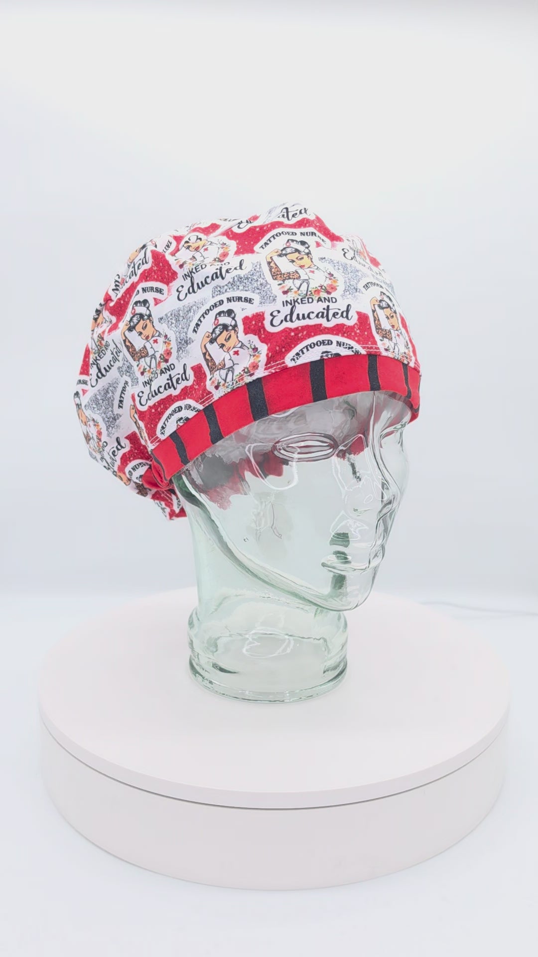 A 360-degree rotating view of a white mannequin head wearing the Tattoo Nurse Full Coverage Scrub Cap. The cap features a vibrant traditional tattoo flash art pattern with text reading 'Inked and Educated' and 'Tattooed Nurse,' finished with a bold red and black striped brim.
