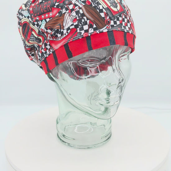 A 360-degree rotating view of a full coverage medical scrub cap on a clear mannequin head, displaying a red 1950s retro diner pattern with checkered accents and classic retro illustrations.