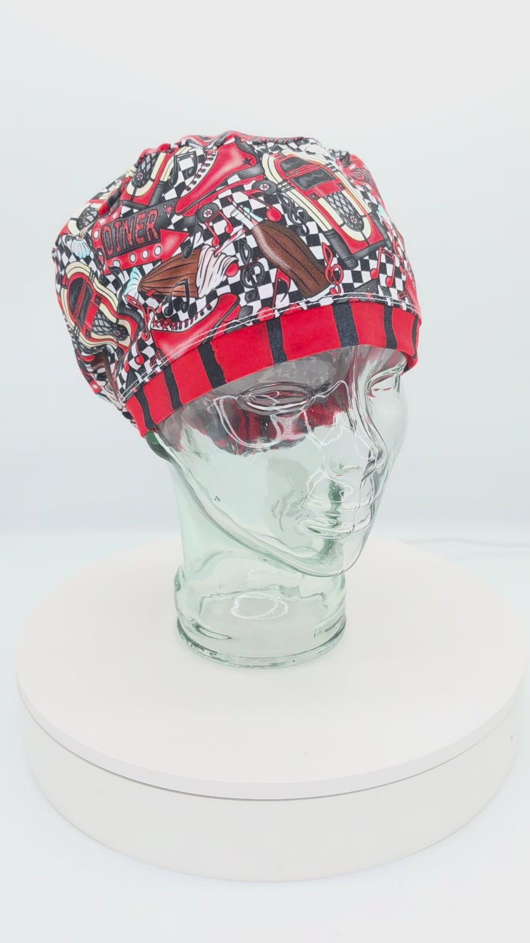 A 360-degree rotating view of a full coverage medical scrub cap on a clear mannequin head, displaying a red 1950s retro diner pattern with checkered accents and classic retro illustrations.