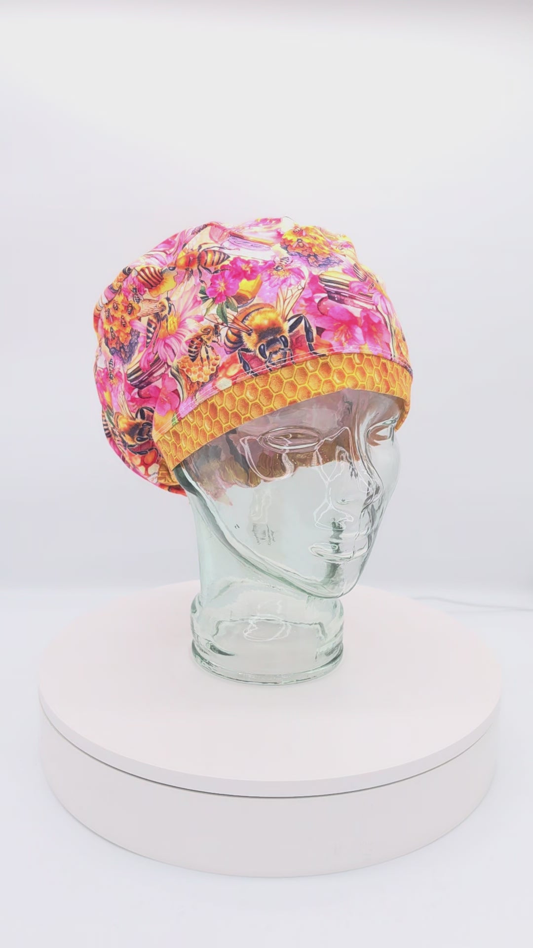 A 360-degree rotating view of a full coverage medical scrub cap on a clear mannequin head, featuring a vibrant orange and yellow bumblebee and honeycomb pattern.