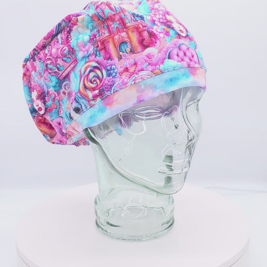 A 360-degree rotating view of a Full Coverage Scrub Cap on a clear mannequin head, displaying a vibrant, colorful pastel candy fairytale pattern with cotton candy clouds and whimsical sweets.
