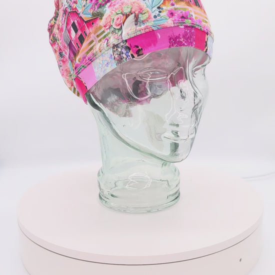 A 14-second rotating product video providing a 360-degree view of the Country Girl Full Coverage Scrub Cap on a clear mannequin head. The medical hat features a vibrant pink fabric patterned with a rustic Western floral and cowgirl motif, finished with a matching solid pink brim.