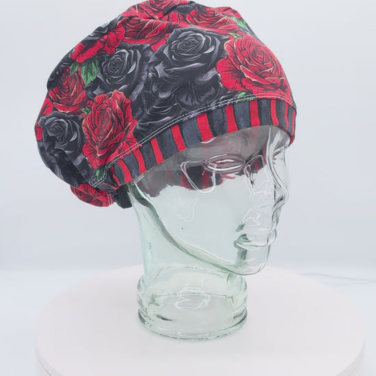 A 14-second rotating product video showing a 360-degree view of the Red and Black Roses Full Coverage Scrub Cap on a clear mannequin head. The medical hat features a dark gothic floral pattern of realistic red, charcoal, and black roses, finished with a bold red and black vertically striped brim.