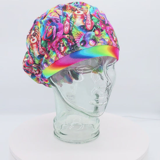 A 360-degree rotating view of the Rainbow Woman Euro-style scrub cap on a glass mannequin head, showcasing its vibrant, multicolored abstract face pattern against a black background and the adjustable back toggle closure.