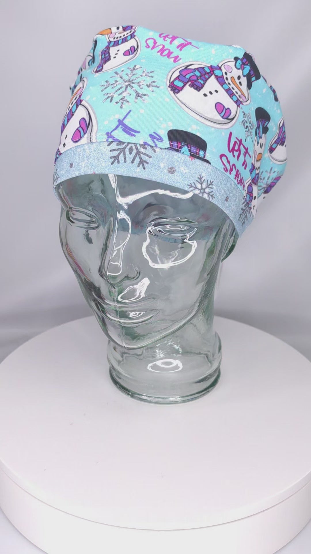 A demonstration video showing the high-quality stretch, adjustable drawstring toggle, and comfortable fit of the "Let it Snow" snowman scrub cap.